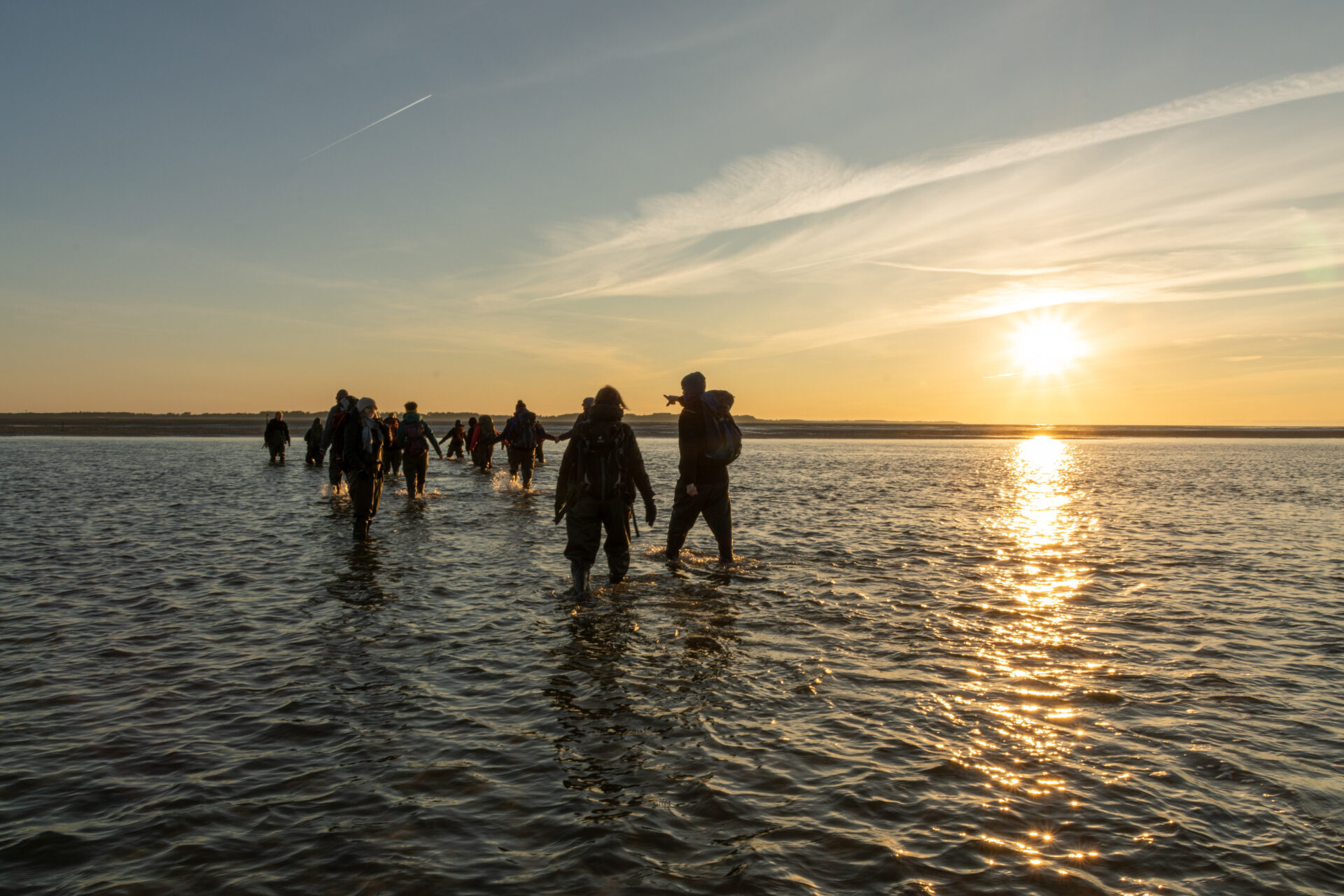 Amrum im Winter entdecken: Eine Gruppe Menschen bei tiefstehender Sonne im flachen Meerwasser