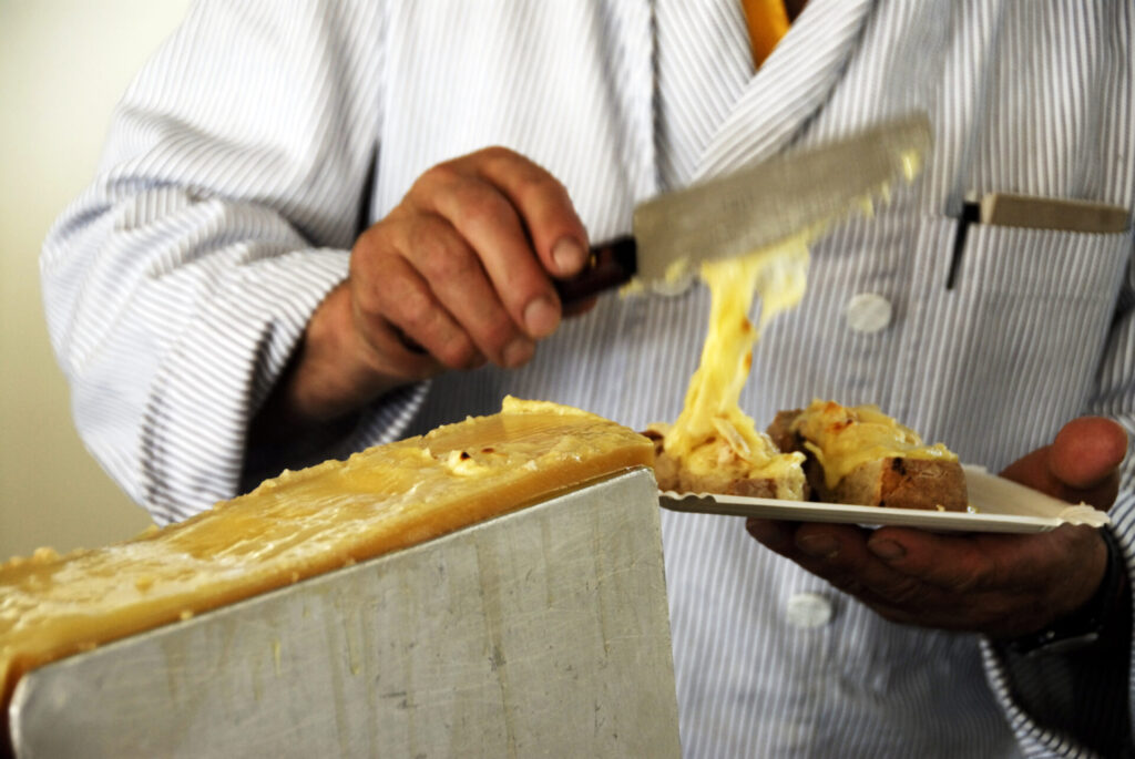 Der Koch kratzt den geschmolzenen Käse auf ein Stück Brot.