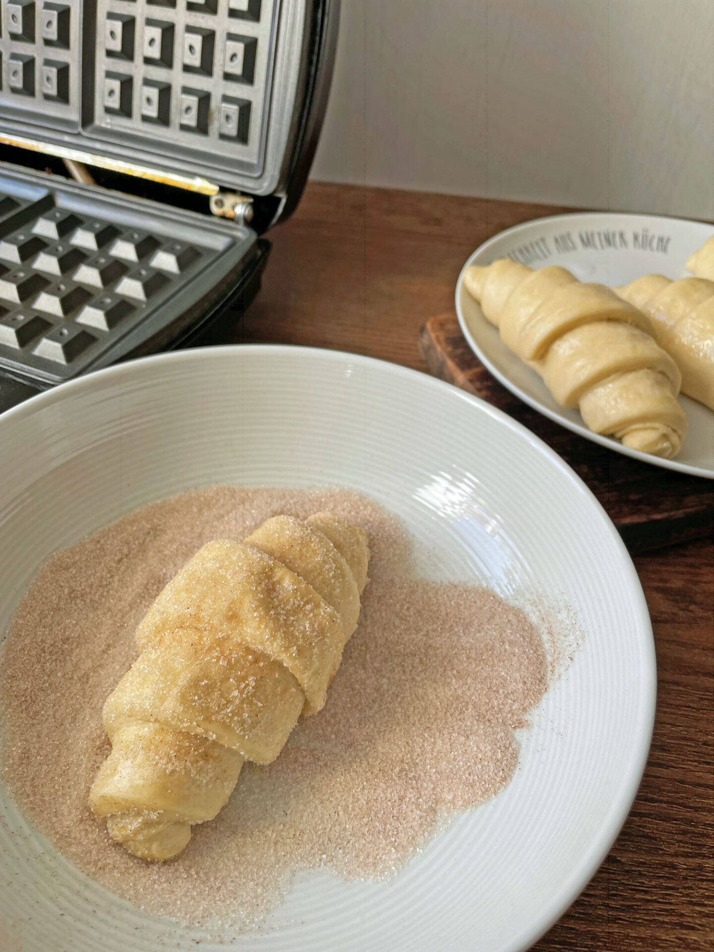 Rohe Croissant-Teiglinge werden in Zimt-Zucker gewälzt, bevor sie ins Waffeleisen kommen