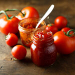Ketchup selber machen ohne Zucker: Zwei Gläser mit rotem Tomatenketchup auf einem Holztisch und mit einigen roten Tomaten