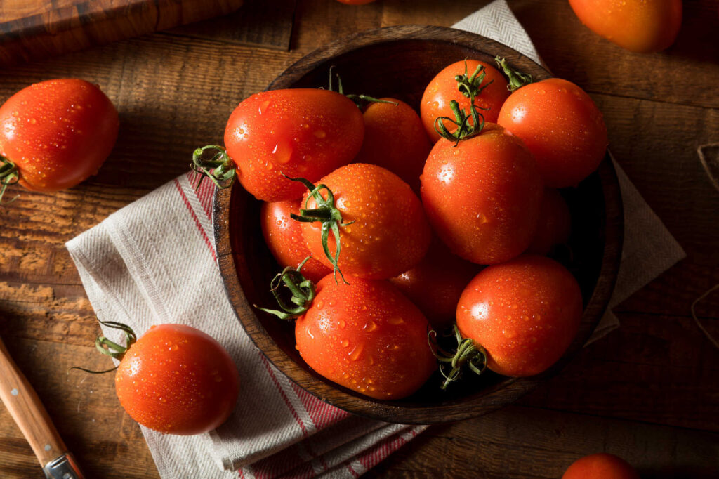 Ketchup selber machen ohne Zucker: Frisch gewaschene Roma Tomaten in einer Holzschale auf einem Holztisch 