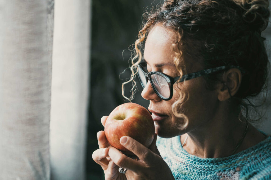 Achtsam essen: Die Frau nimmt den Apfel mit allen Sinnen wahr während sie am Fenster steht