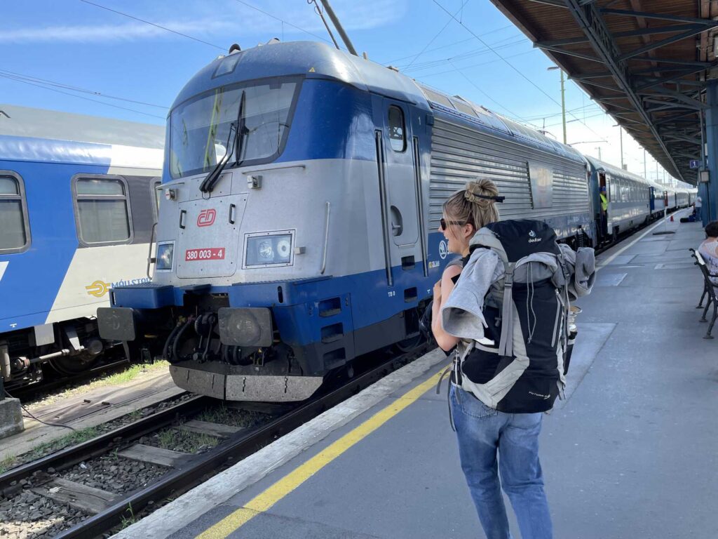 Mit dem Nachtzug reisen: Frau mit Reiserucksack am Bahnsteig, im Hintergrund ein Zug