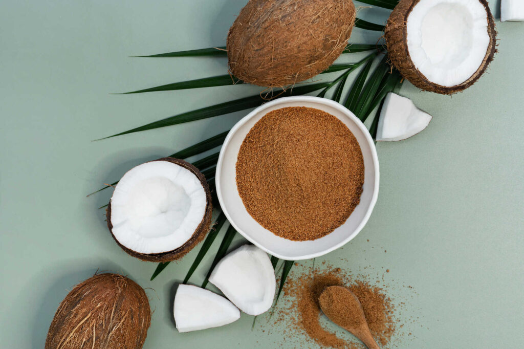 Zuckeralternative: braun-krümeliger Kokosblütenzucker neben einer offenen Kokosnuss